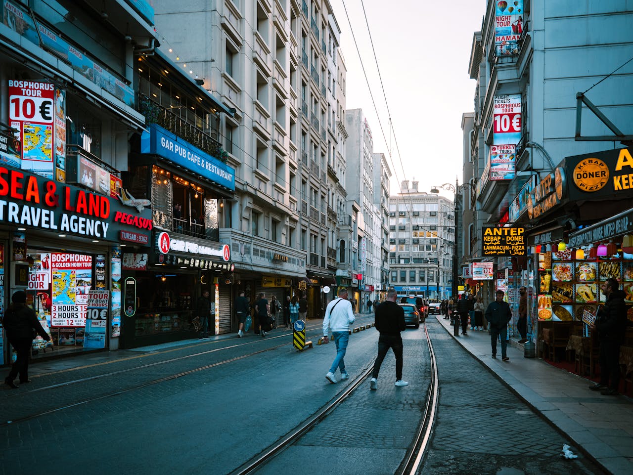 about-us Vibrant street scene in Istanbul featuring shops, people, and tram tracks under a clear sky.